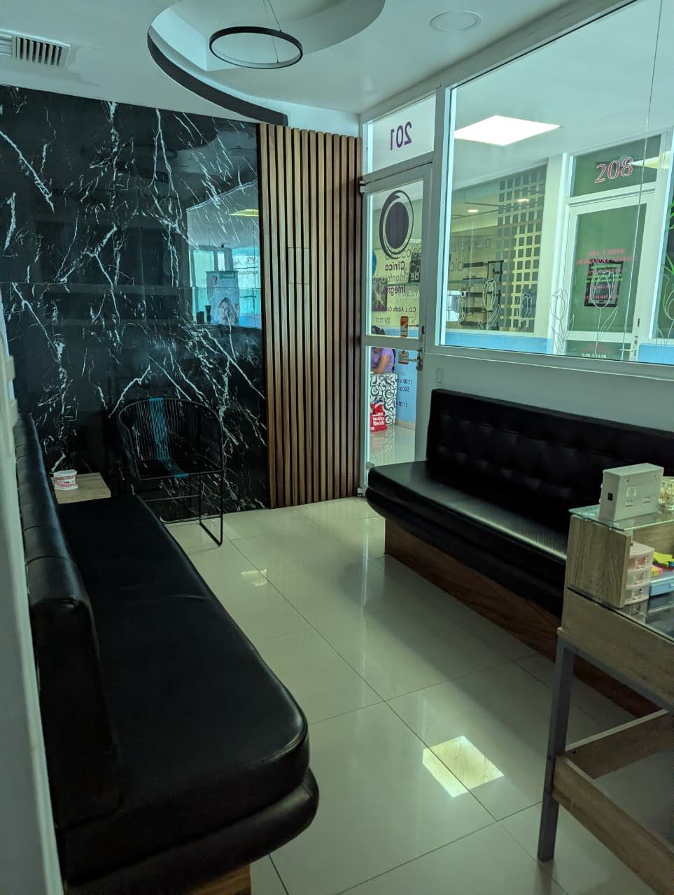 Recepción del consultorio con sofás negros, pared de mármol y paneles de madera